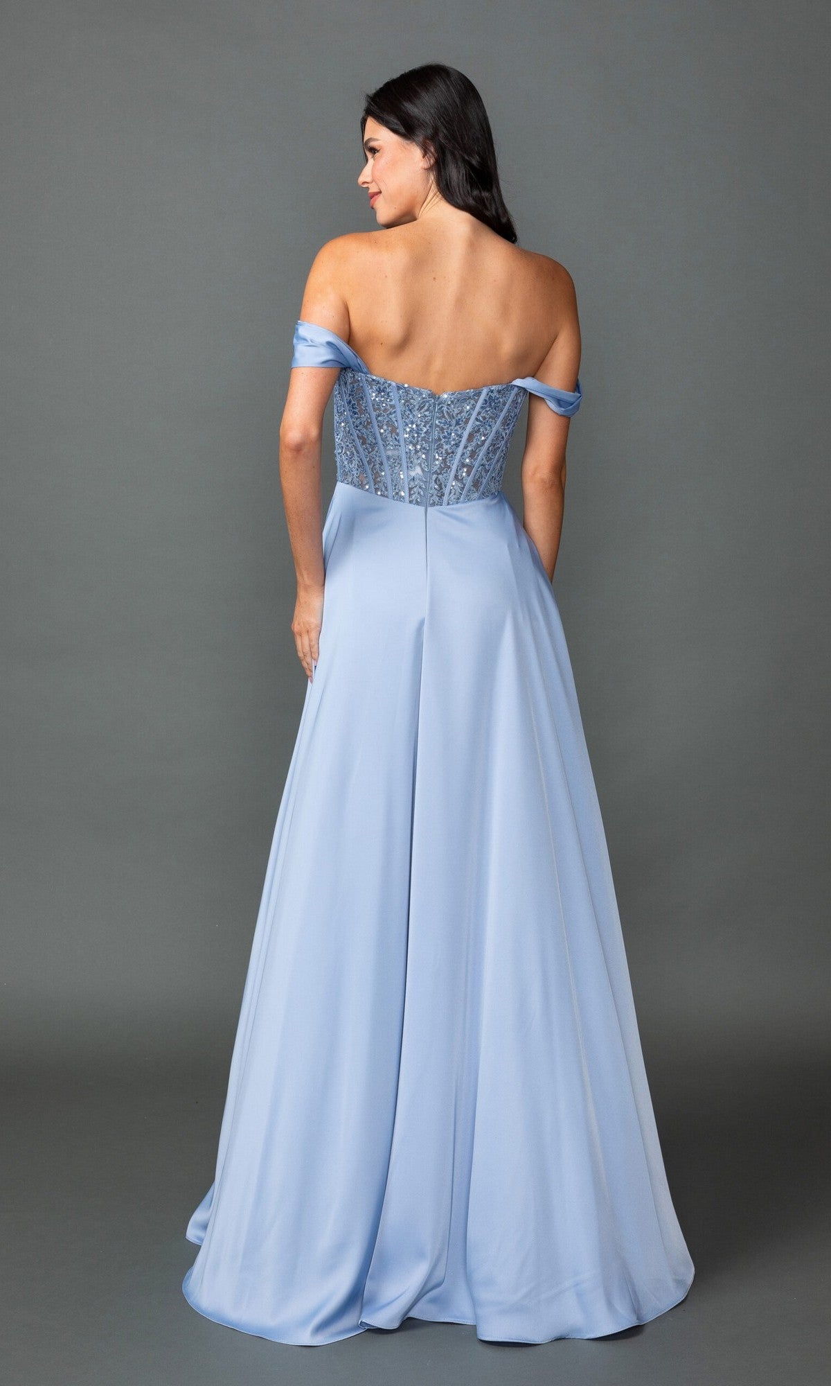Woman in the Off-Shoulder Corset Prom Gown: Dancing Queen 4546A, featuring a light blue off-the-shoulder design with an embellished corset bodice and flowing skirt, stands with her back to the camera against a plain background.